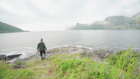 挪威塞格拉島 (senja island) 的一個男人走向岩石海岸,拿着一根<unk>去釣魚.