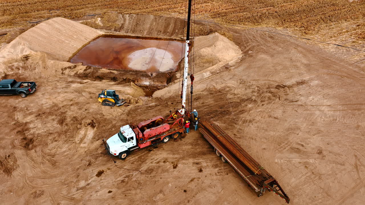 Three workers stand at the truck with drilling tower. Approaching the team of people installing oil producing equipment in the field.