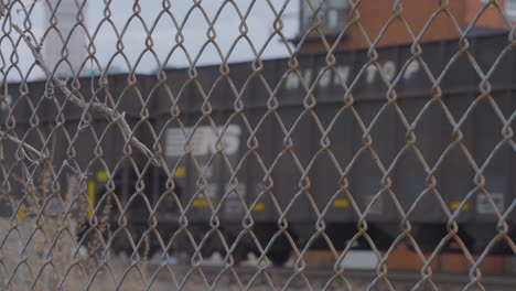 train-cars-and-oil-tankers-passing-through-shot-from-behind-chain-link-fence