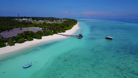 tourist boat heads to jetty on tropical maldives island, aerial dolly back 4k