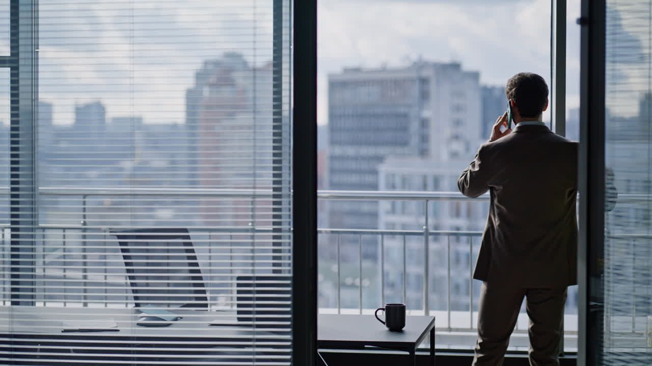 Primo piano di un capo preoccupato che parla al cellulare in un ufficio con vista sulla città indossando un elegante abito