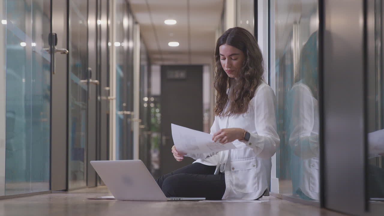 joven mujer de negocios sentada en el piso en el corredor de una oficina moderna trabajando en una computadora portátil