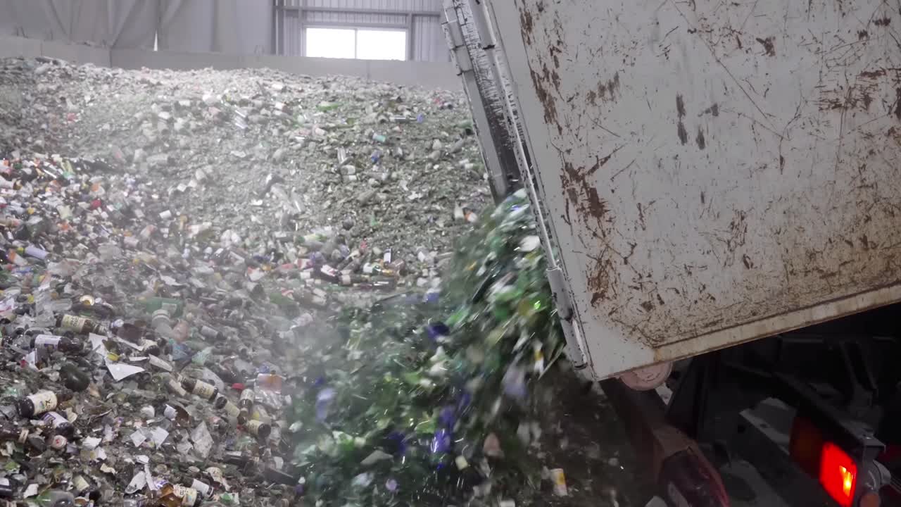 A truck dumps broken glass bottles on the ground. Creating new materials from recycled glass.