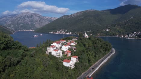 kotor bay, montenegro, drone shot of buildings and church on cape above sea and ferry line boats in kamenari