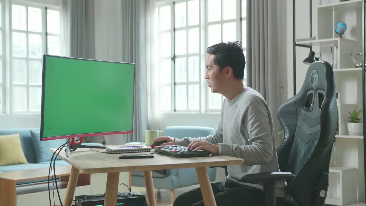 Asian Man In Long Sleeved T-Shirt And Black Pants With Green Screen Desktop Computer Being Happy Successful In Work While Working At Home.