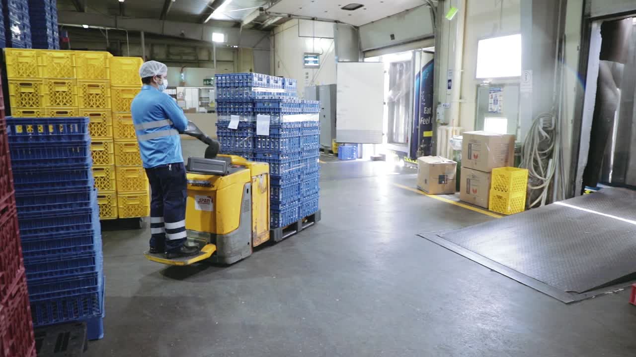 Man with mask driving automatic pallet truck for transporting goods in factory.Tracking shot.