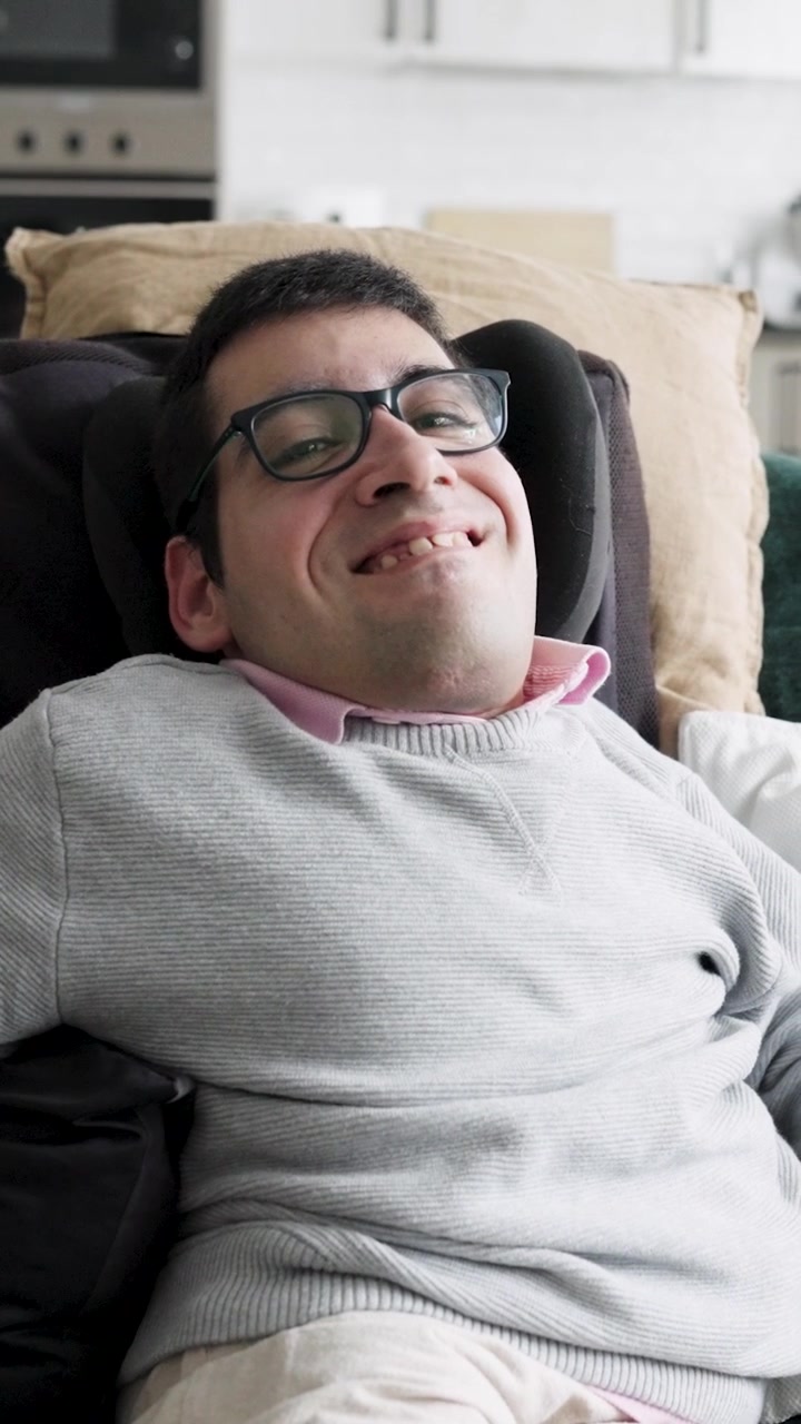 Giovane uomo con gli occhiali che sorride seduto su una sedia a rotelle