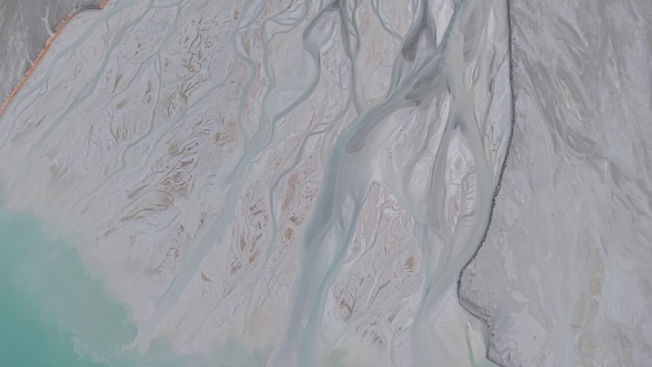 Aerial drone shot of braided river channels flowing through light-colored sediment into turquoise water