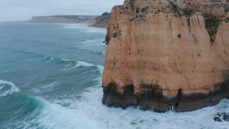 La-Inclinación-Del-Dron-Aéreo-A-La-Vista-Aérea-De-Los-Pájaros-Revela-Fuertes-Olas-Que-Se-Estrellan-Contra-El-Acantilado-Rocoso-De-La-Costa-En-Lagos,-Portugal