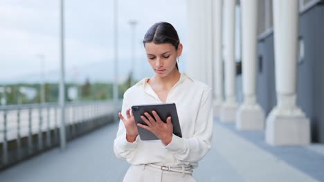 Businesswoman-sitting-outside-modern-building-walking-working-on-tablet