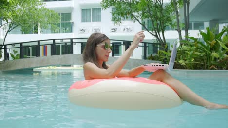female freelancer sits in an inflatable circle in the pool and throws the laptop into the water. busy during the holidays. the concept of remote work. selective focus