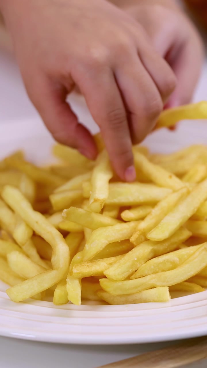 Close-up child hand picking golden french fries from plate, soft indoor lighting, static camera