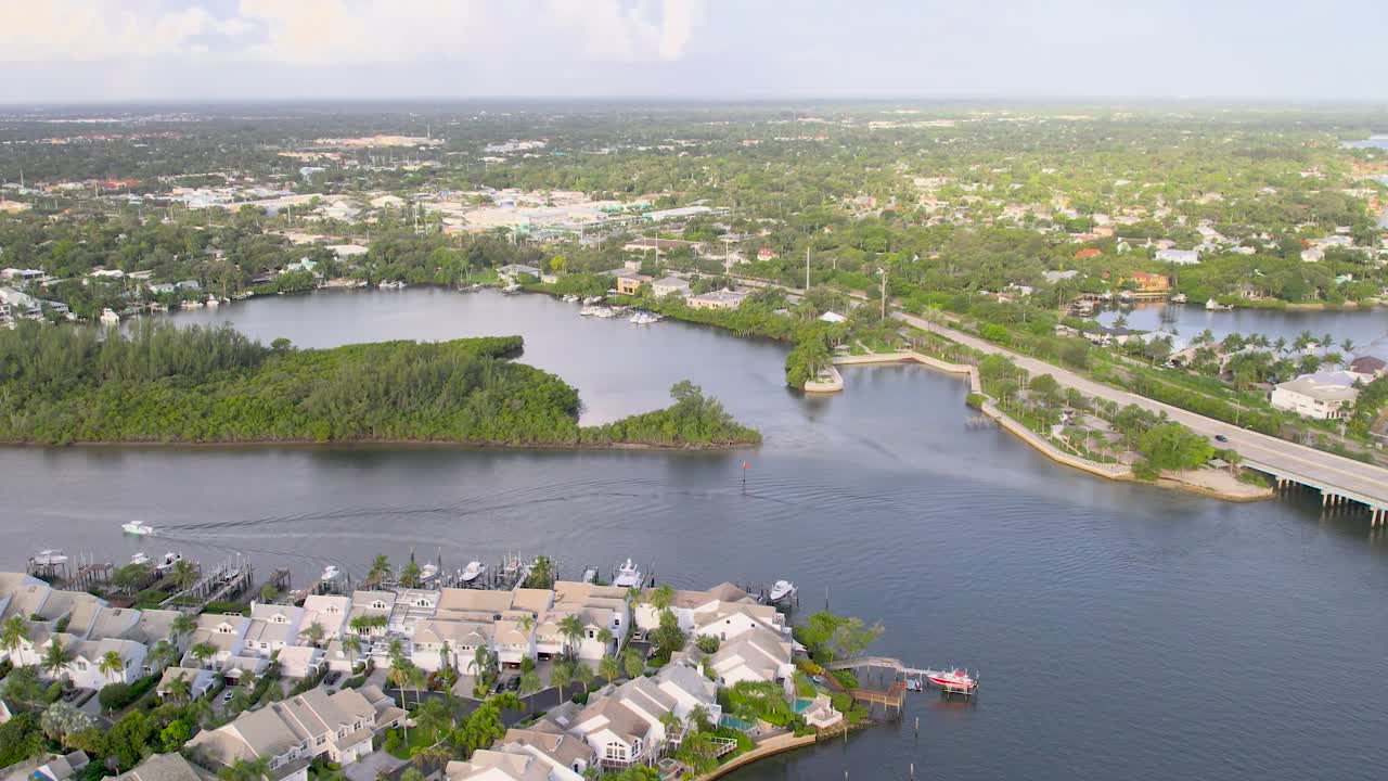 Aerial view of a scenic waterfront community with homes lining the shores of a calm lake, surrounded by lush greenery and open skies in Jupiter, Florida