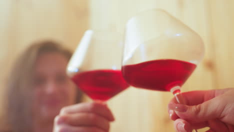 blurred silhouettes of women raising wine glasses in toast against warm wooden wall background, gentle focus on celebratory gesture, convivial mood evoked through soft blur