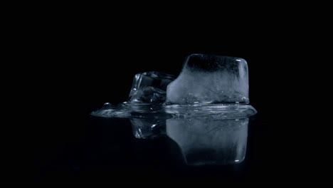 static timelapes shot of melting cold ice cubes on a reflective black surface against black background