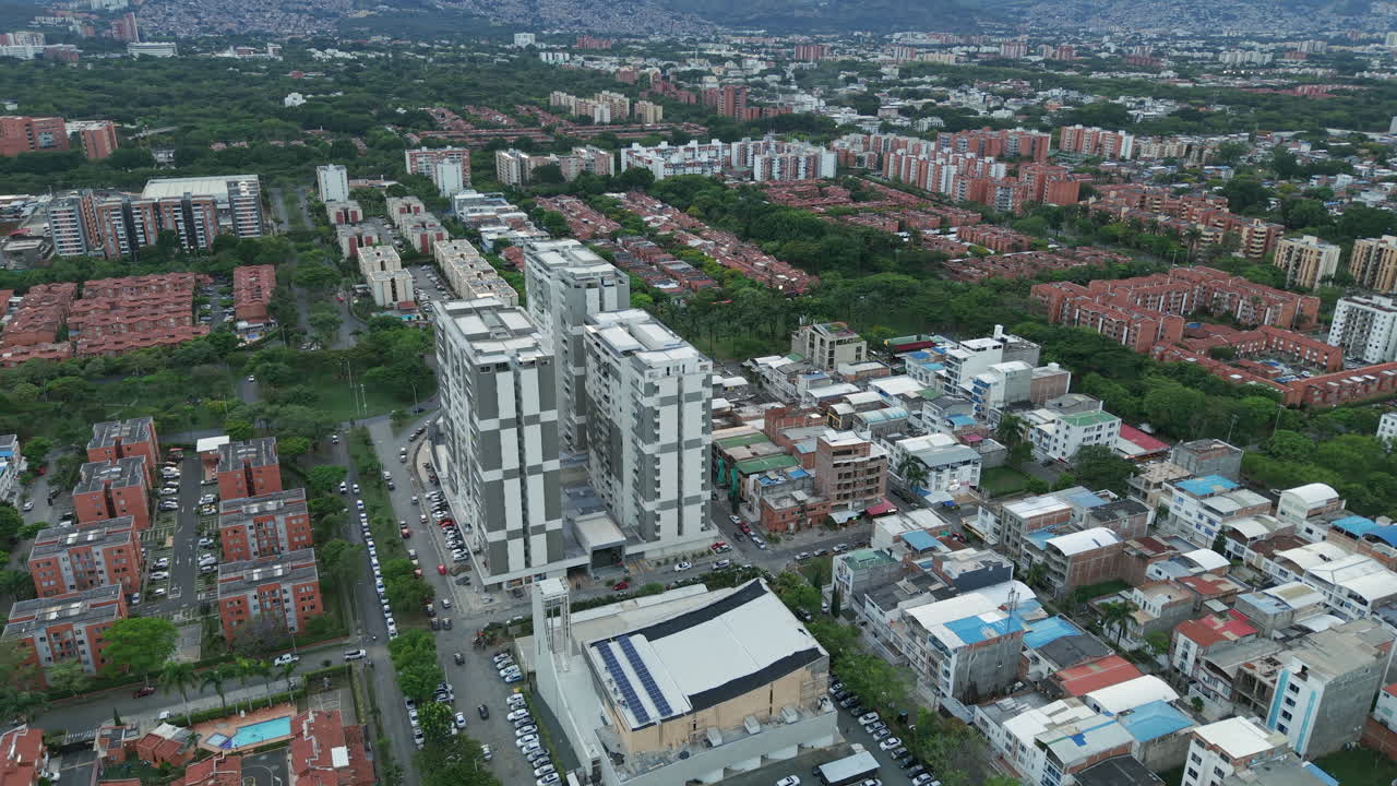 Drone video capturing Valle del Lili's urban sprawl with vibrant cityscape, modern architecture, dense buildings, lush greenery, under soft daylight, providing a broad view