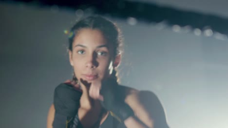 young caucasian sportswoman with braided pigtails doing shadow fight in boxing ring and looking at the camera