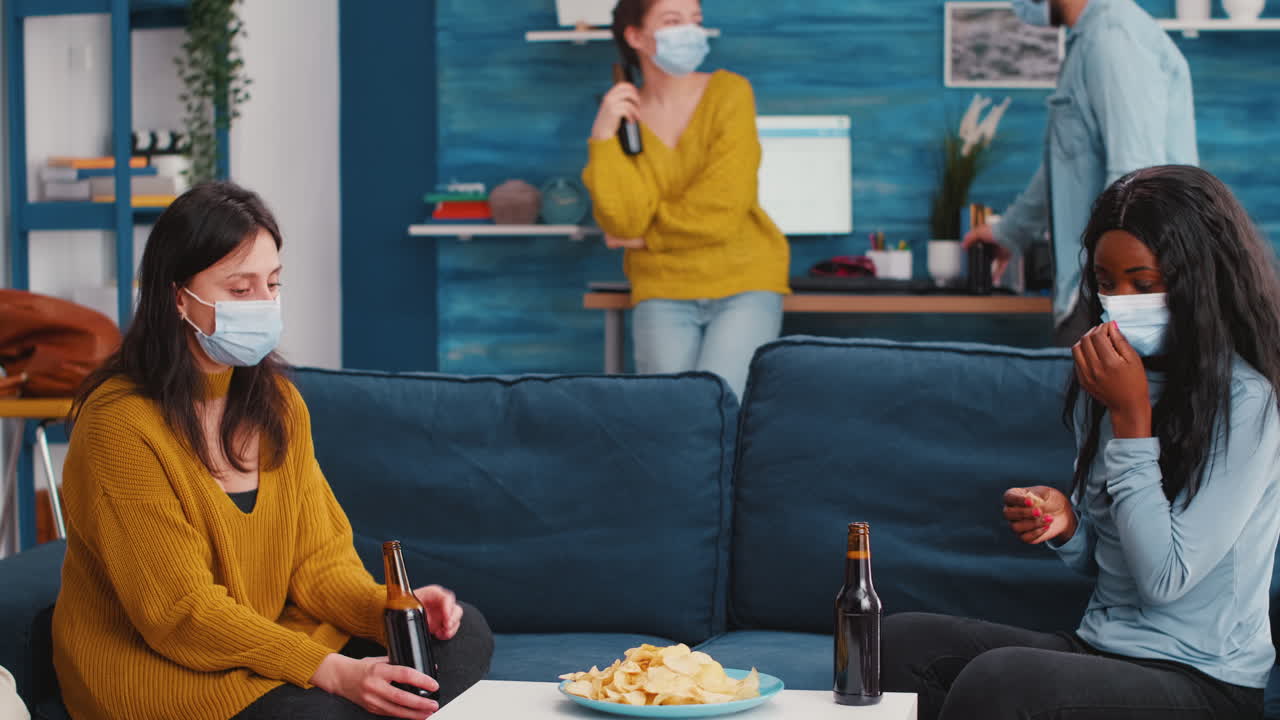 Women sitting on sofa discussing taking off protective mask eating snacks