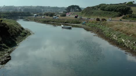 Aerial-low-view-along-calm-river-stream-over-static-white-boat-near-roadside