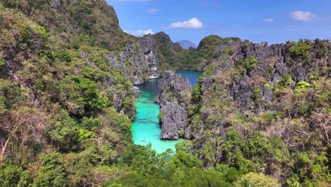 Aerial descent into Big Lagoon on Miniloc Island, revealing steep limestone karsts, dense tropical foliage, and brilliant blue waters within the Bacuit Archipelago in northern Palawan