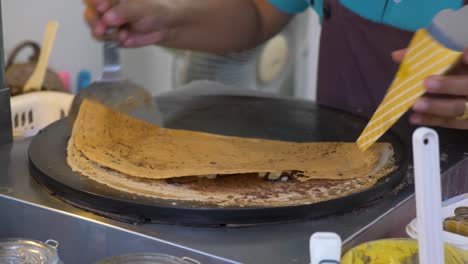 slow motion: chef finishing up pancake, folding it up and putting it into the holder, dream world, thailand