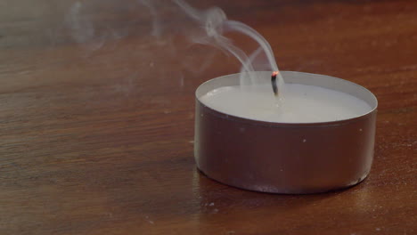 Extreme-close-up-of-tea-candle-on-table-being-blown-out,-smoke-curls