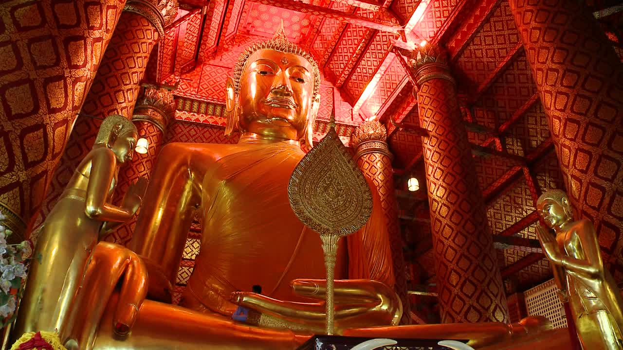 Worshippers at a Golden Buddha temple in Bangkok, Thailand. Camera tilts up to the Buddha. There is one craftsman working on the statue.