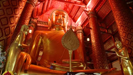 worshippers at a golden buddha temple in bangkok, thailand. camera tilts up to the buddha. there is one craftsman working on the statue.