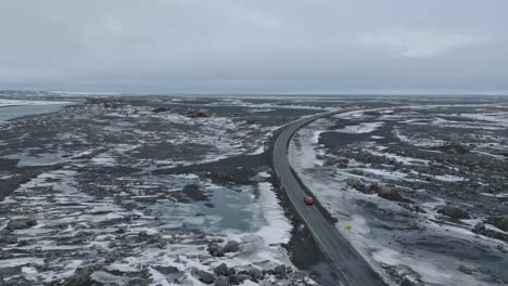 Drohnenaufnahme-Eines-Autos,-Das-Sich-Während-Der-Späten-Wintersaison-Auf-Nasser-Straße-In-Der-Isländischen-Landschaft-Bewegt