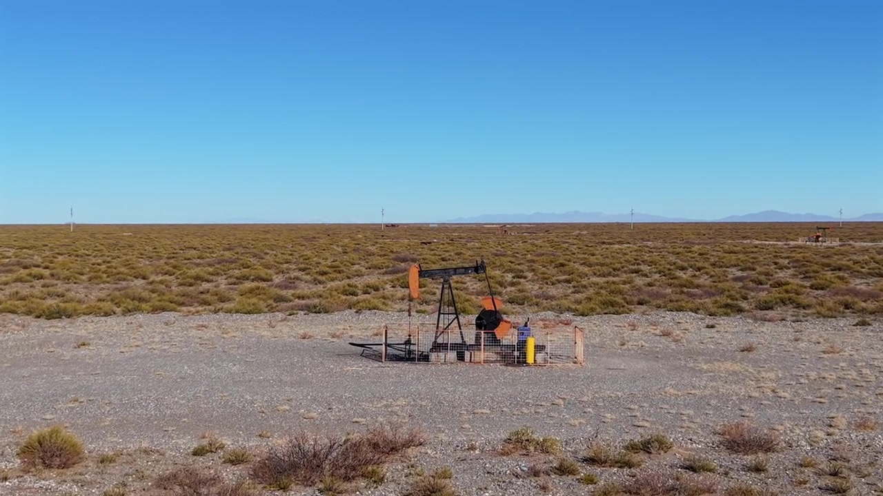 Avvicinamento aereo frontale verso un bilanciere di estrazione di petrolio greggio attivo in funzione in un campo arido con le Ande in lontananza sotto il sole di metà mattina/mezzogiorno