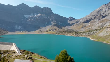 Aerial-view-of-the-shores-of-Lac-de-Salanfe-in-Valais,-Switzerland-on-a-sunny-autumn-day-in-the-Swiss-Alps-with-a-view-of-an-alpine-landscape,-mountain-peaks,-cliffs-and-hydroelectric-dam