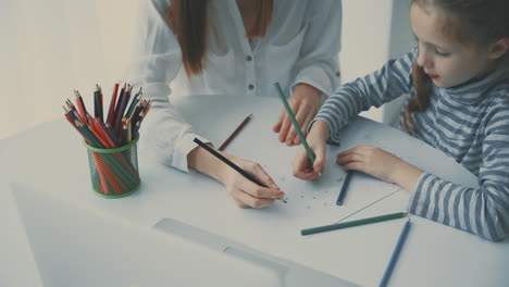 young woman helps little girl to do homework with colored pencils