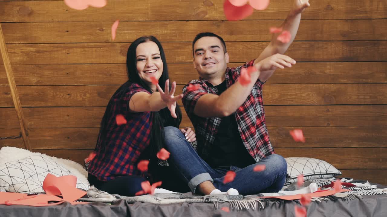 Casal apaixonado jogando corações de papel no quarto e se beijando no Dia dos Namorados.
