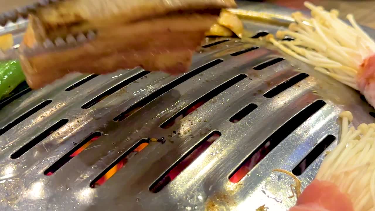 Metalltenger snur tykke skiver av svinebuk sammen med enoki-sopp og paprika på en grill
