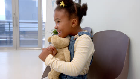 happy african american girl sitting in hospital waiting room and holding mascot, slow motion