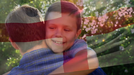 animation of english flag over happy caucasian father and son embracing in sunny garden