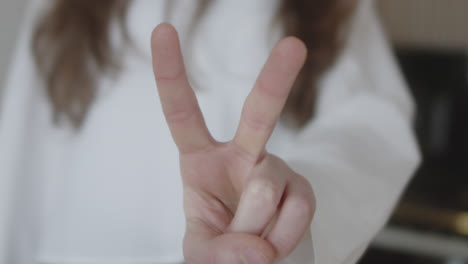 beautiful slow motion close-up shot of a young caucasian woman's fingers raising her index and middle finger forming a “v” and “love and peace” in a white shirt at home in natural light.