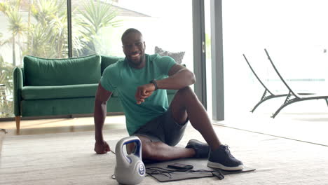 strong and fit man sitting on floor with kettlebell and smartphone, smiling