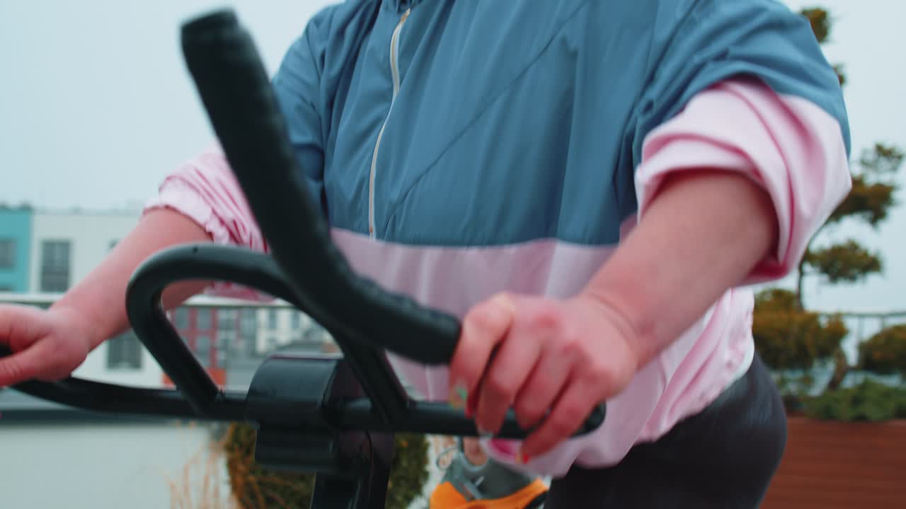 건강한 백인 여성이 집 옥상 체육관에서 고정된 자전거 기계 자전거에서 운동을 하고 있습니다.