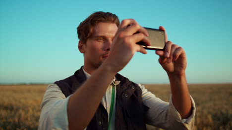 farmer holding smartphone at harvest field. focused agriculture worker portrait.