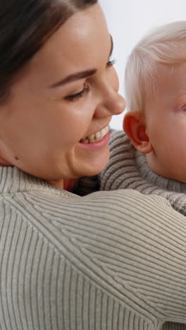 Blue-eyed blond infant in mom&#039;s hands. Cute baby touching and clapping male hand. White backdrop. Vertical video