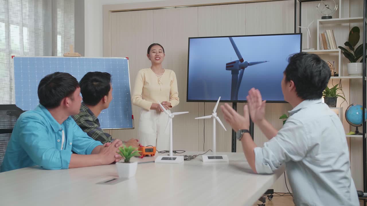 태양전지를 가진 아시아 여성 엔지니어가 사무실에서 풍력 터빈에 대한 프레젠테이션을 성공시켰고, 관객들은 박수를 치며 인상적이라고 느습니다.