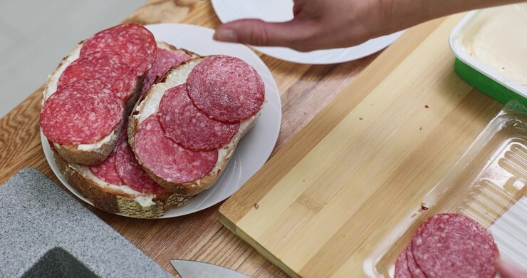 Woman places homemade salami sandwich onto plate in kitchen