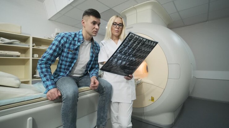 Woman doctor radiologist explains the results of MRI scanning for young male patient, showing the snapshot with images, observing and analyzing mri scan in modern clinic beside modern closed-type MRI