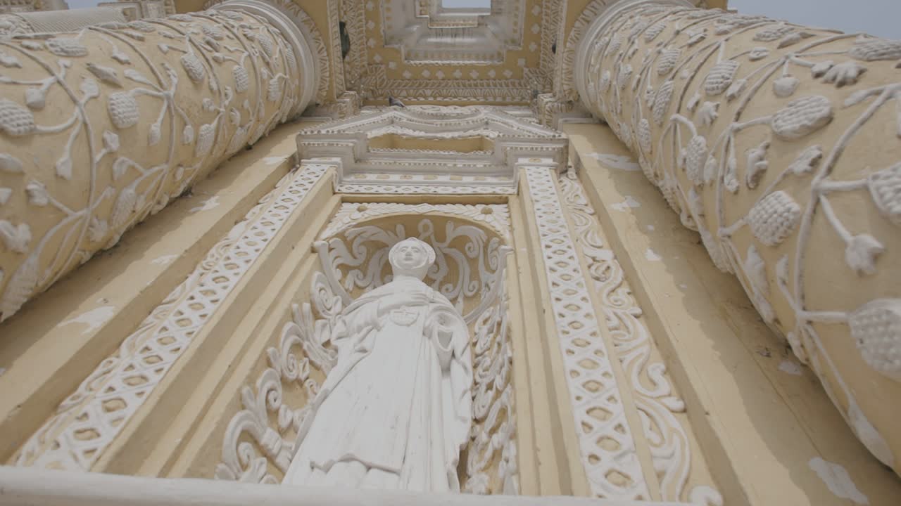 과테말라 안티구아에 있는 교회 앞에 있는 성자의 조각상을 가로질러 이동합니다.