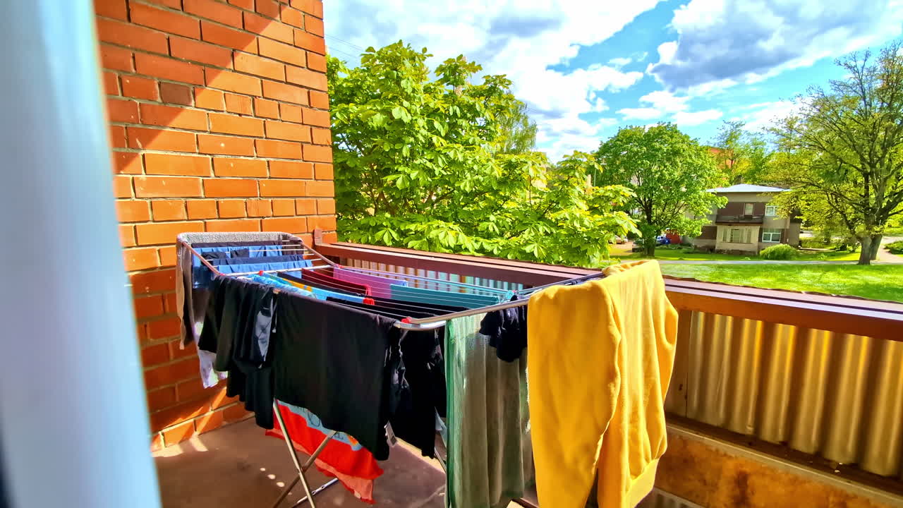 Colorful clothes dry in the sun on a small balcony with cloudy blue sky in background