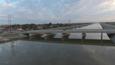 A-drone-flying-above-water-advances-towards-cars-driving-over-a-bridge