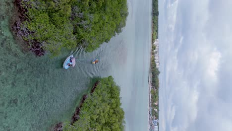 Toma-Vertical-De-Un-Dron-De-Una-Lancha-Rápida-Tirando-De-Un-Bote-Banana-Con-Un-Turista-Divirtiéndose-En-La-Bahía-De-Santo-Domingo-Durante-El-Día-Nublado