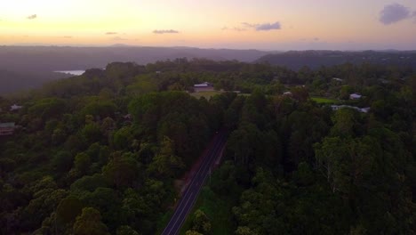 Rising-aerial-shot-of-a-tropical-forest-valley-with-road-and-hills-at-sunset