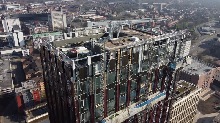 Volo aereo con drone attorno al tetto di una nuova torre in sviluppo su Oxford Road nel centro di Manchester, con vista sugli edifici circostanti della città.